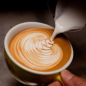 Barista creating latte art on long coffee with milk. Latte art in coffee mug. Barman pouring fresh coffee